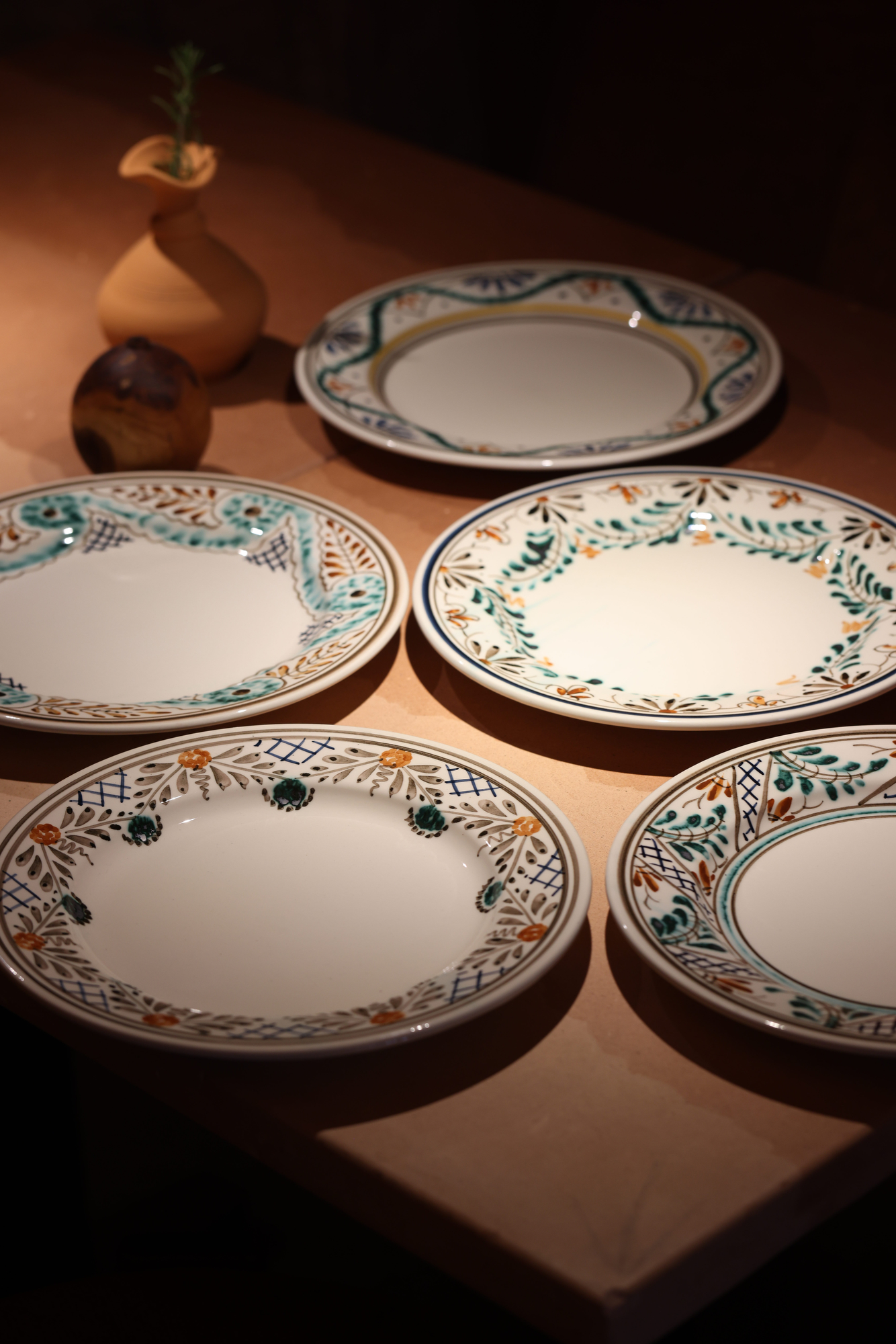 Pratos de louça pintada à mão sobre mesa de pedra, com jarro de barro e azeitona