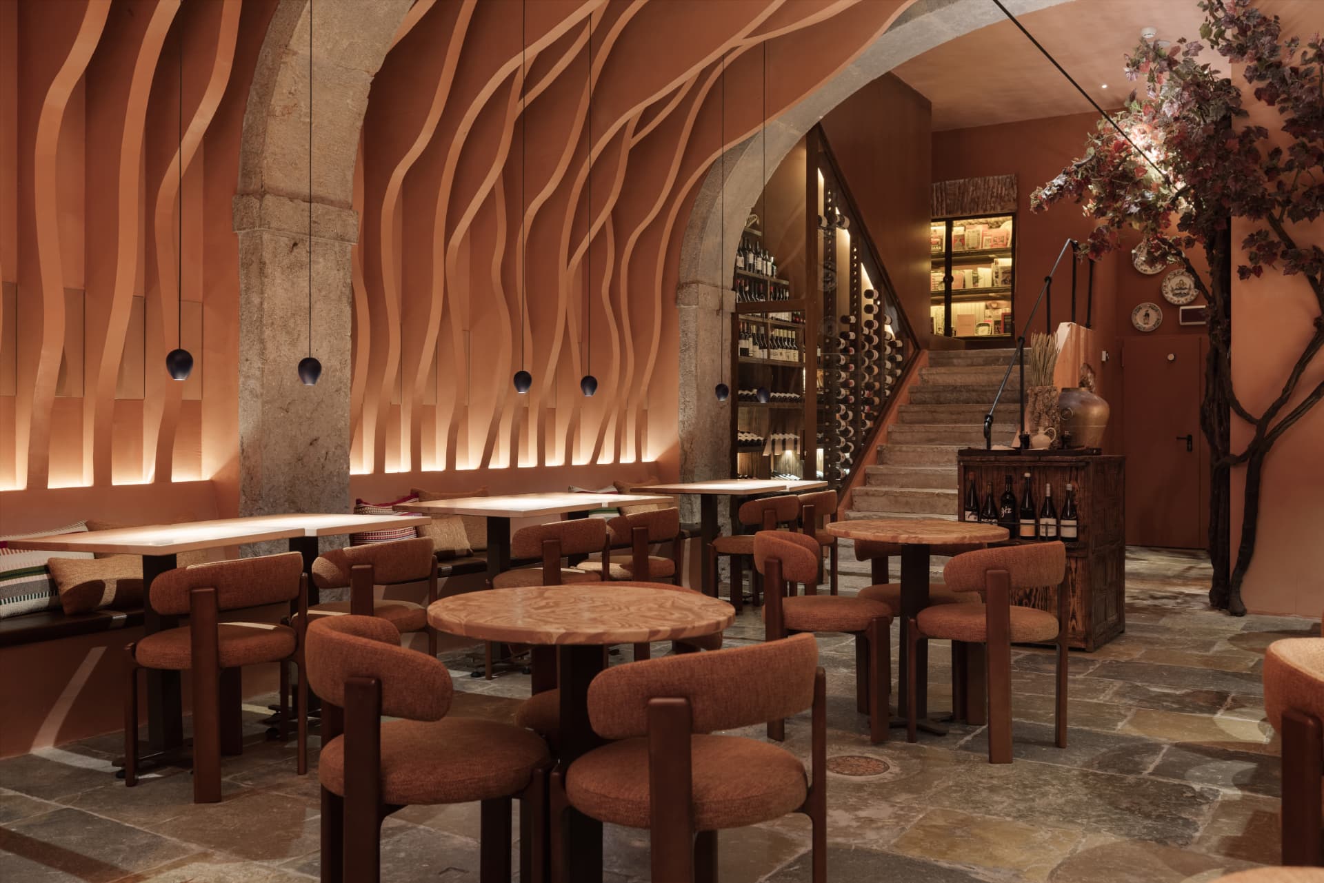 Sala do Origem com arcos de pedra, paredes em ondas de luz quente, escadaria e garrafeira